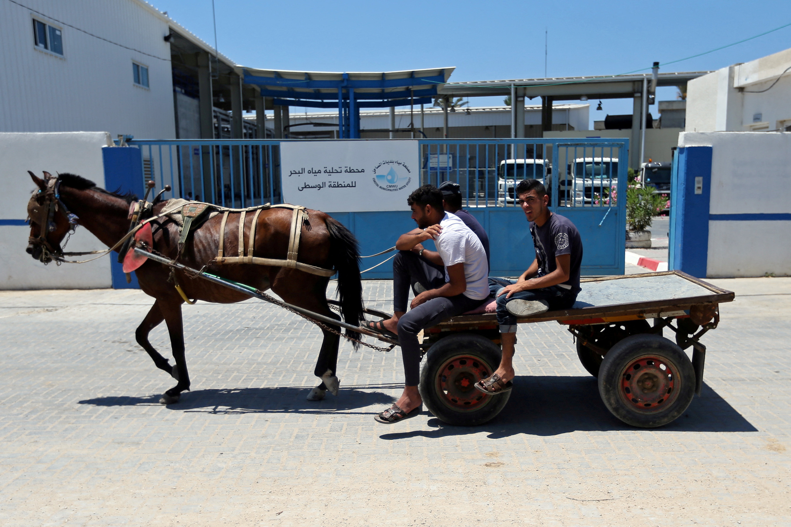 FILE PHOTO: Palestinians ride a horse-drawn cart past Gaza desalination plant, in the central Gaza Strip