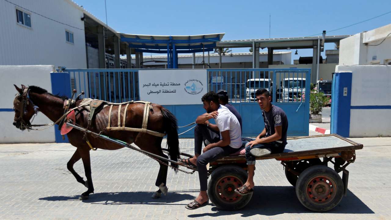 FILE PHOTO: Palestinians ride a horse-drawn cart past Gaza desalination plant, in the central Gaza Strip