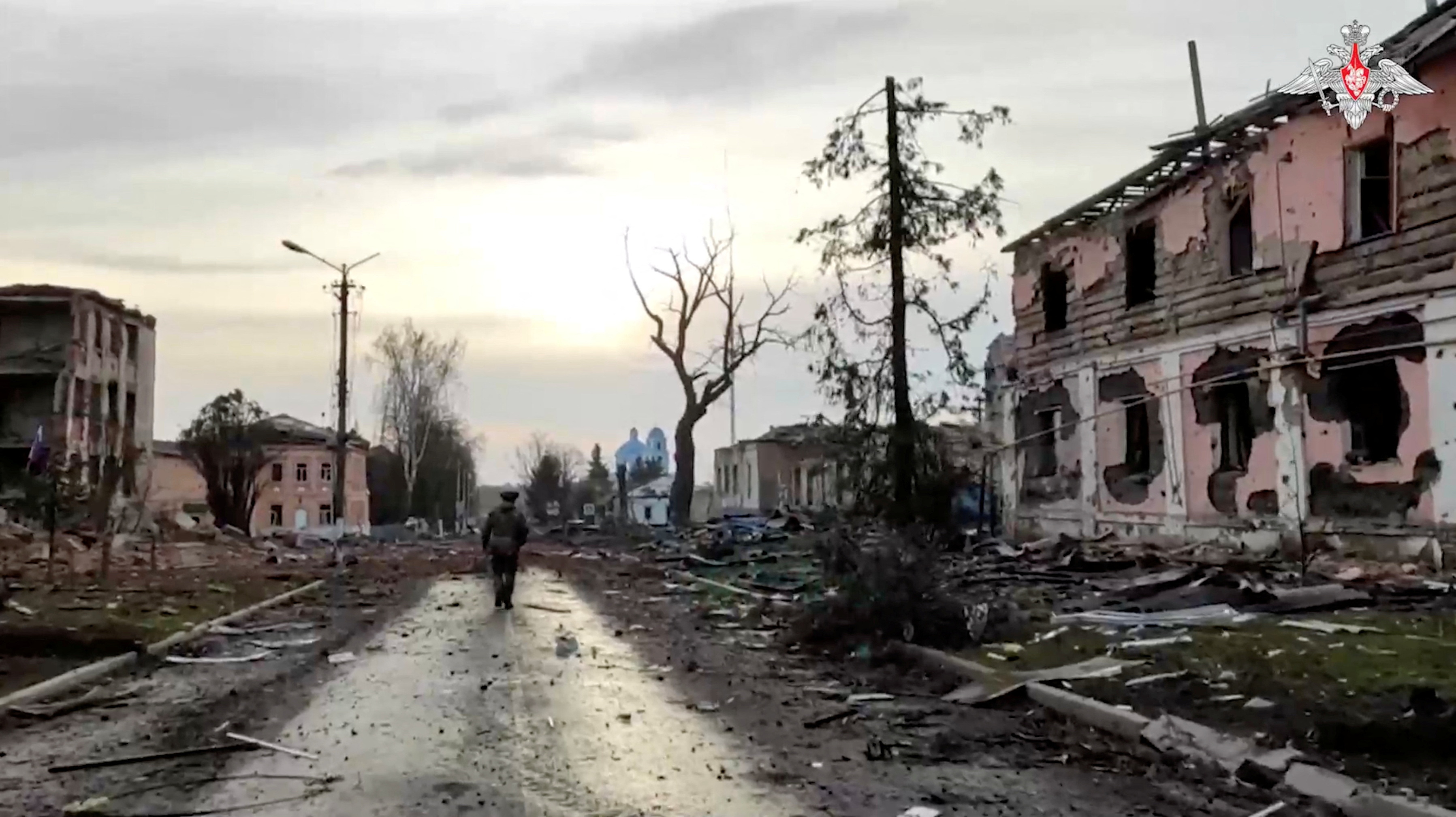 A Russian service member walks past destroyed buildings in Sudzha