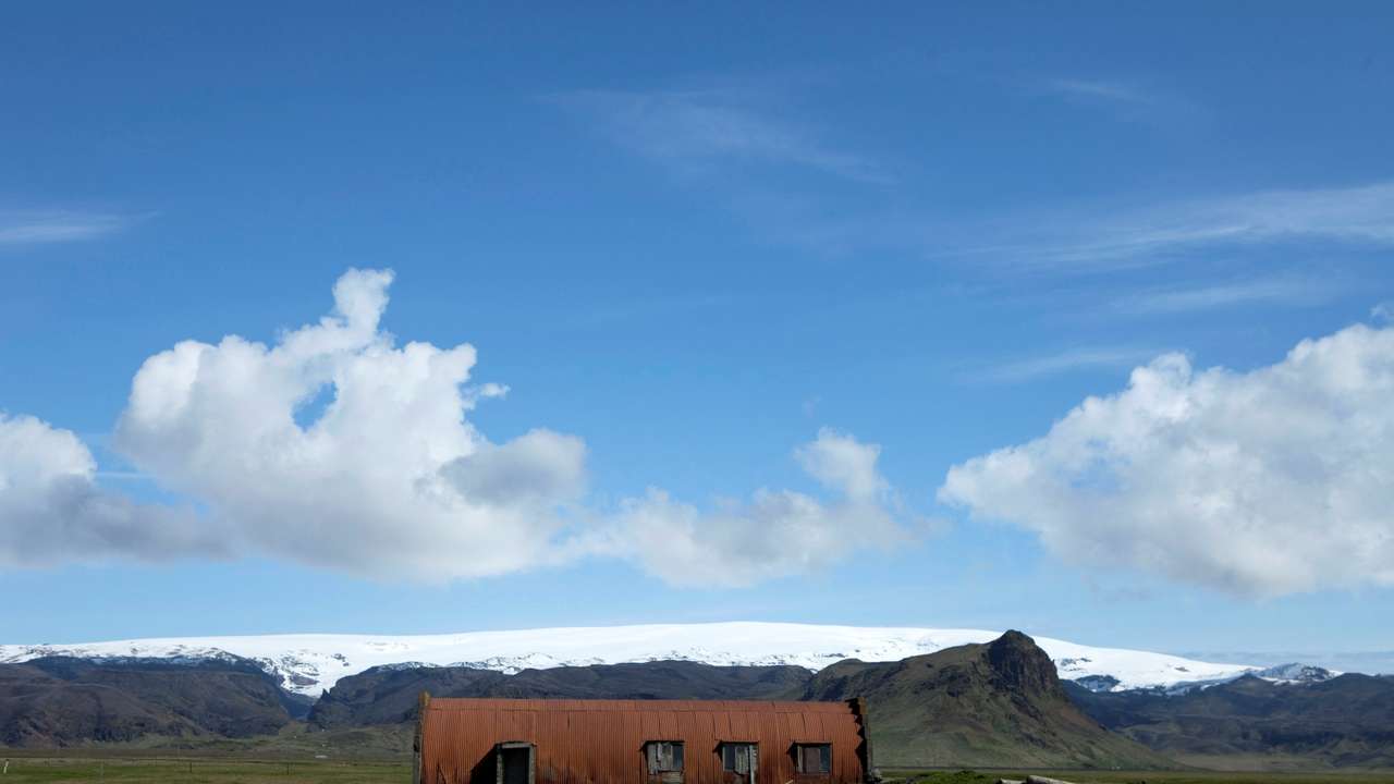 FILE PHOTO: A farm building stands in a field below the Myrdalsjokull glacier that covers the Katla volcano in Evindarholar, Iceland