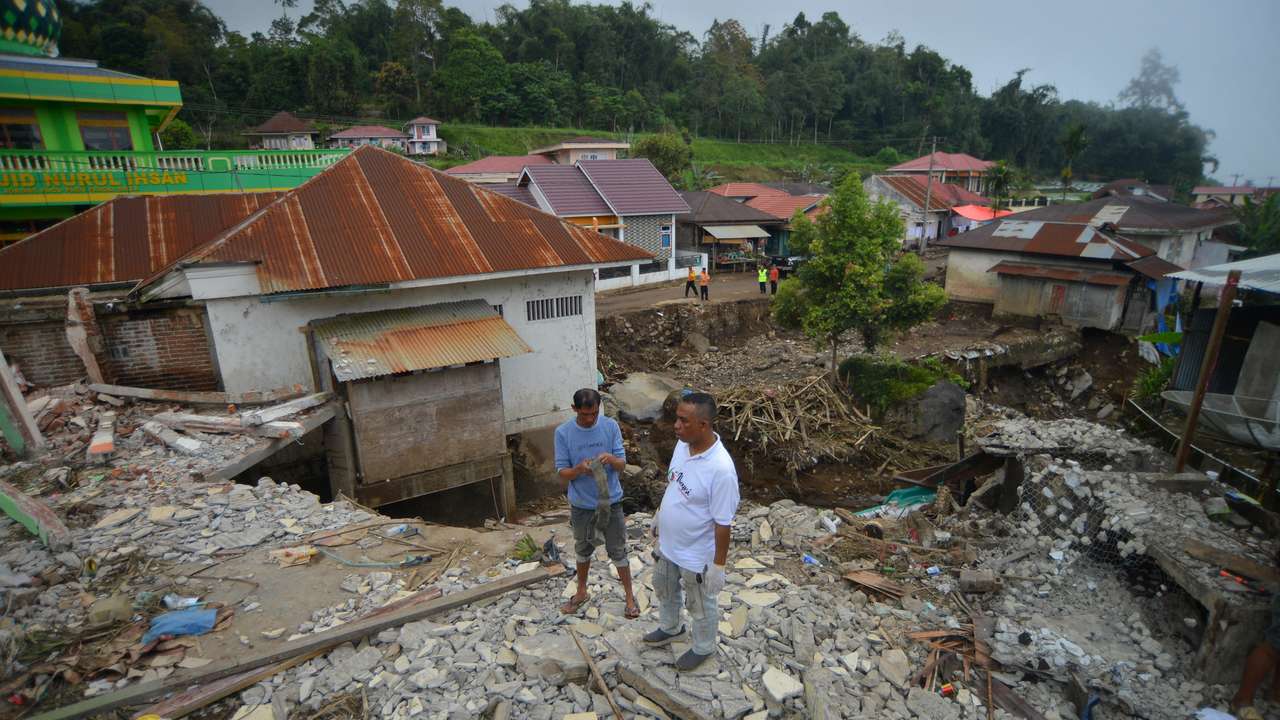 Men stand near a damaged house in an area affected by heavy rain brought flash floods in Tanah Datar