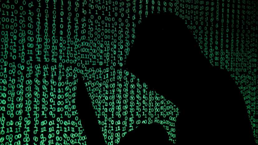 Hooded man holds laptop computer as cyber code is projected on him in this illustration picture