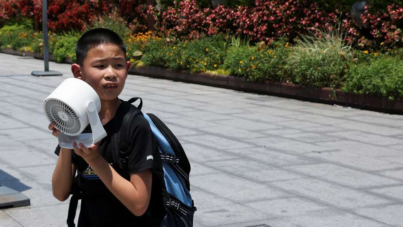 A child holds a portable fan amid a yellow alert for heat, in Shanghai