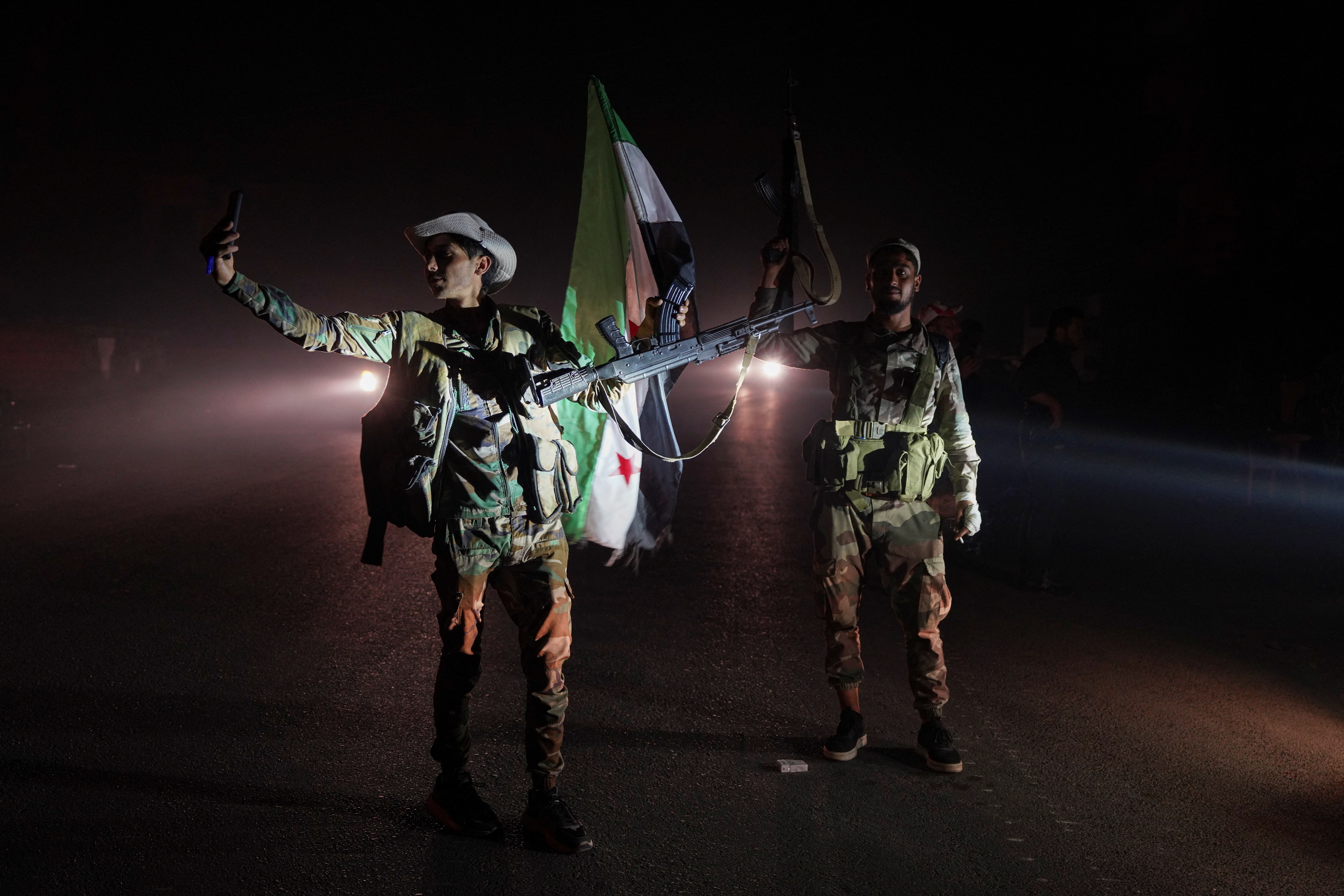 Members of Syrian security forces stand on a road as vehicles transporting other Syrian security forces make their way out of the predominantly druze city of Sweida