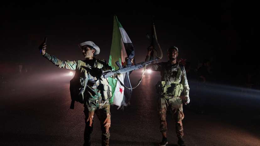 Members of Syrian security forces stand on a road as vehicles transporting other Syrian security forces make their way out of the predominantly druze city of Sweida