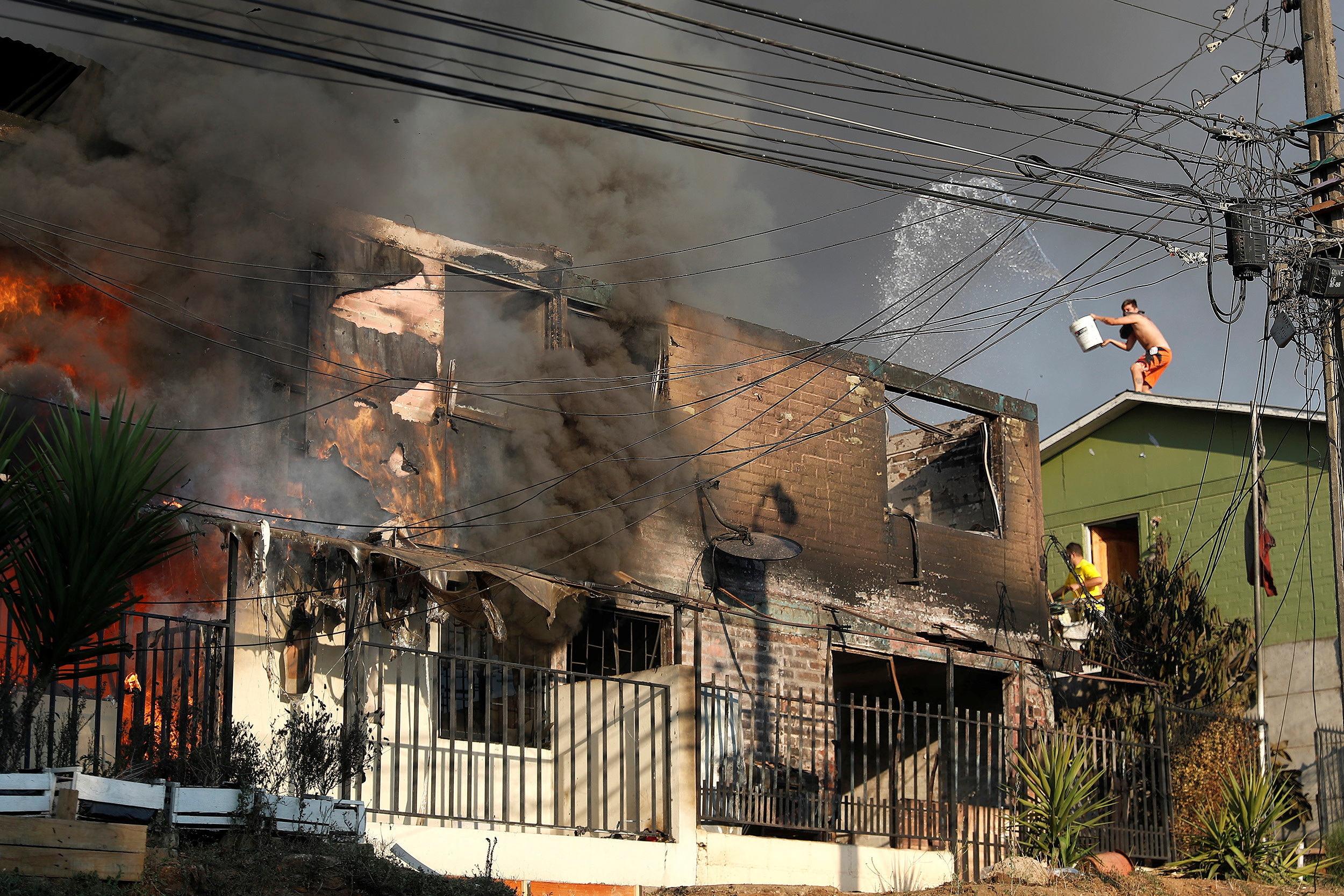 People try to extinguish a fire burning a house during the spread of wildfires in Vina del Mar