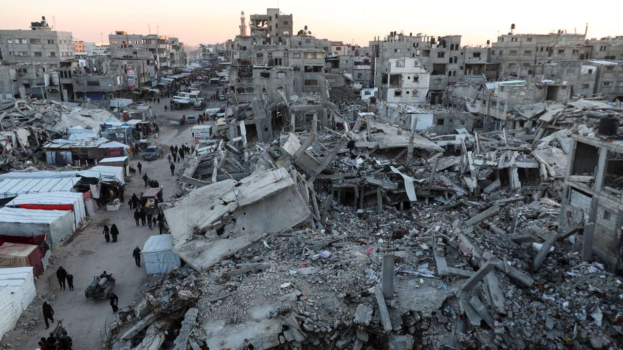 Palestinians walk among the rubble of buildings, In Khan Younis