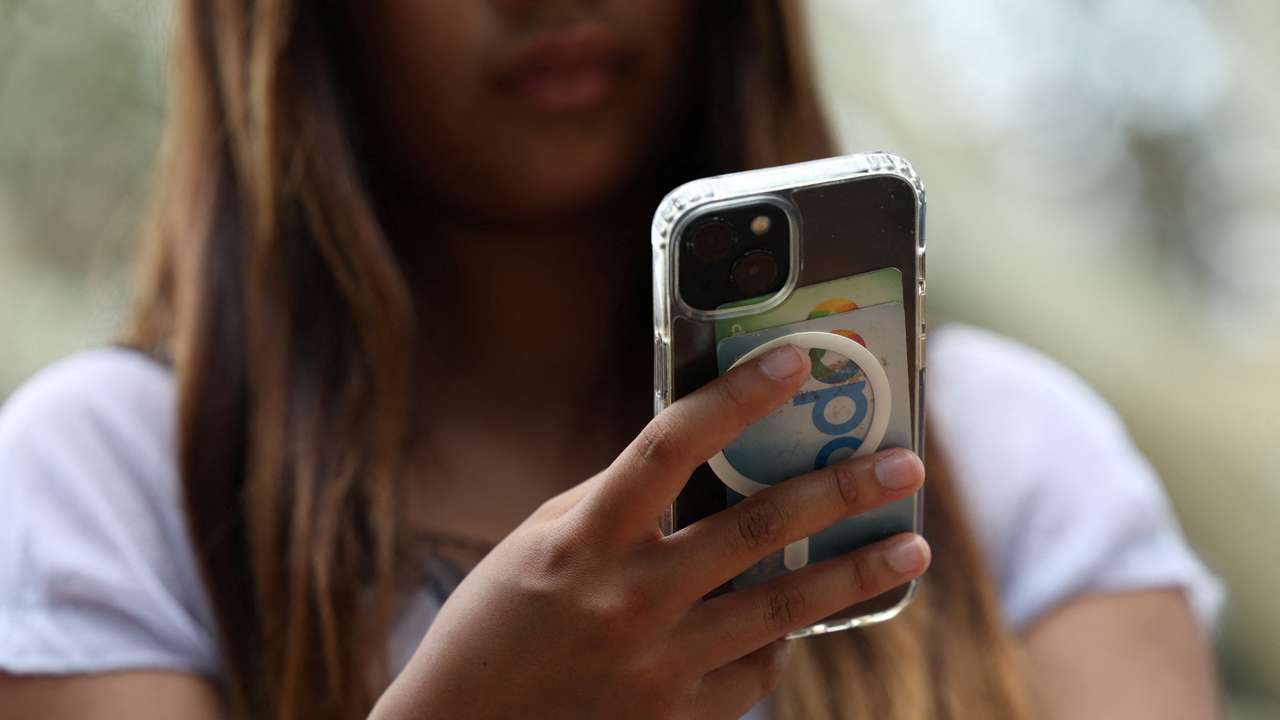 A teenager poses holding a mobile phone as law banning social media for users under 16 in Australia takes effect, in Sydney
