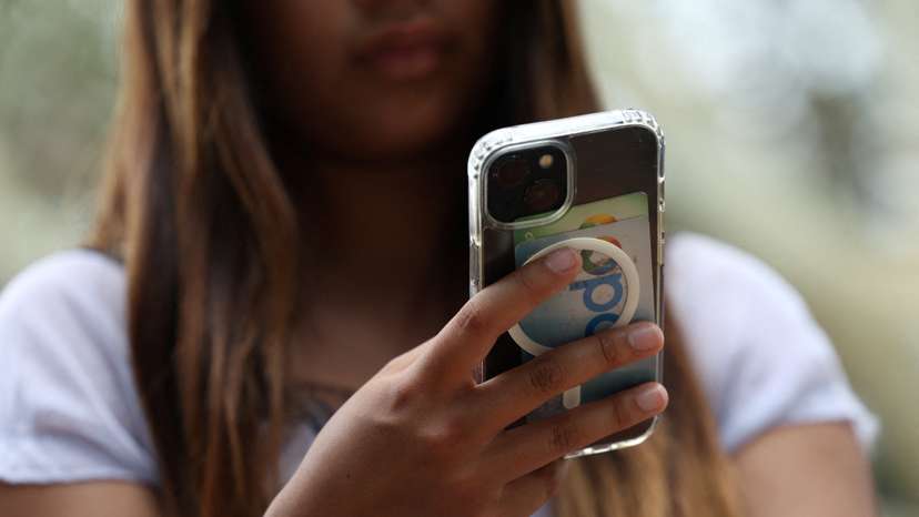 A teenager poses holding a mobile phone as law banning social media for users under 16 in Australia takes effect, in Sydney