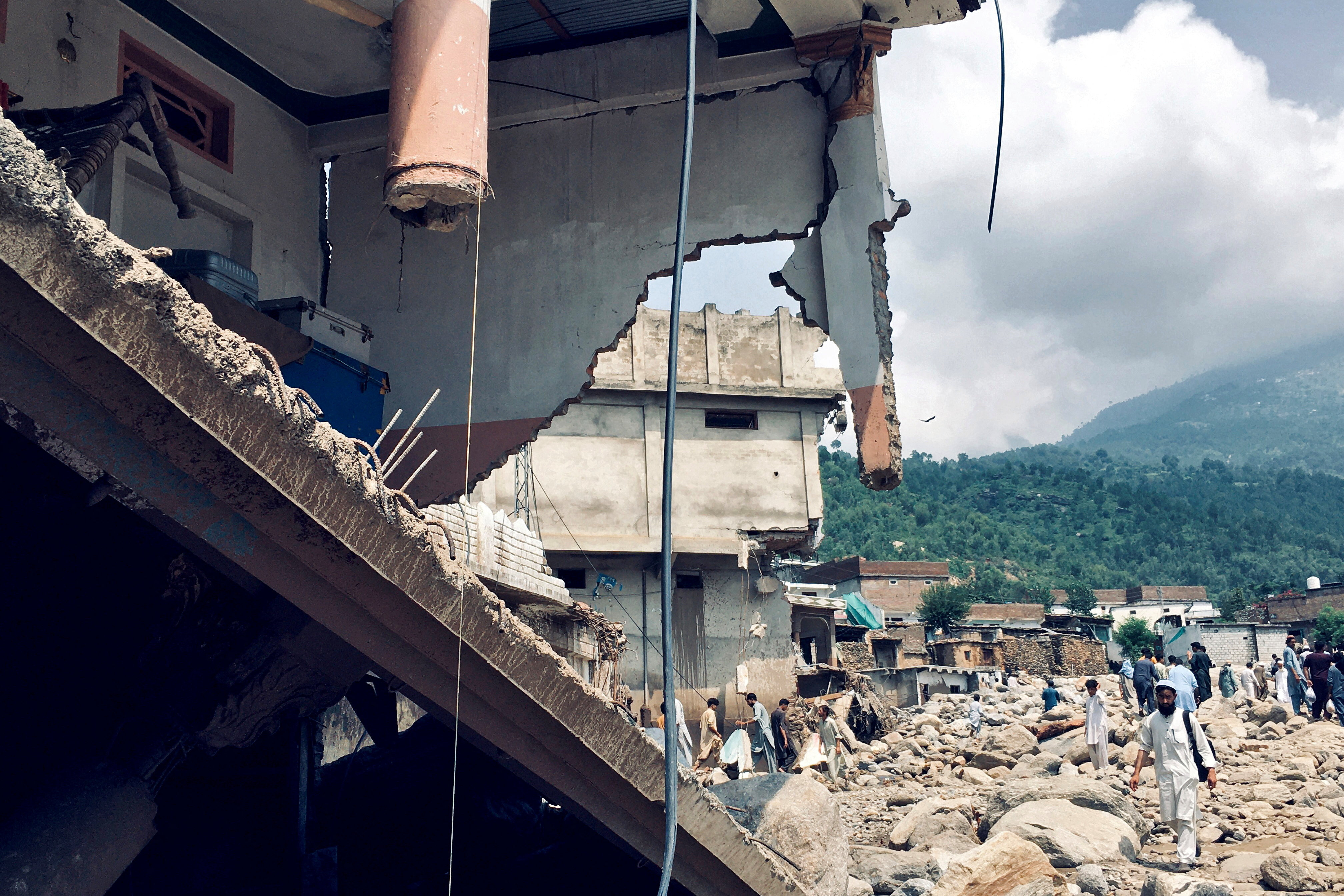 Men walk past damaged houses following heavy rain and floods in Buner district