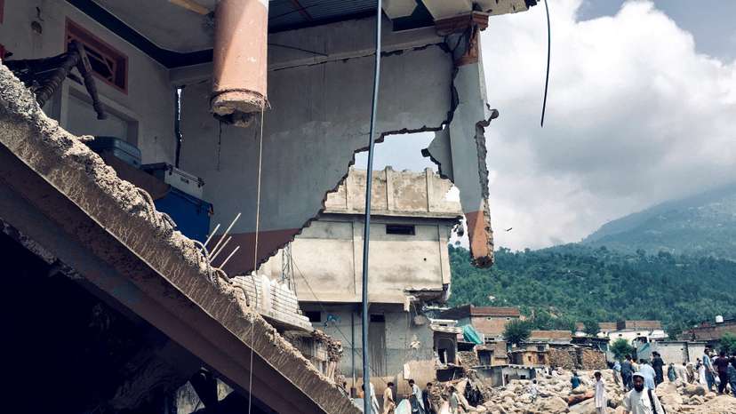 Men walk past damaged houses following heavy rain and floods in Buner district