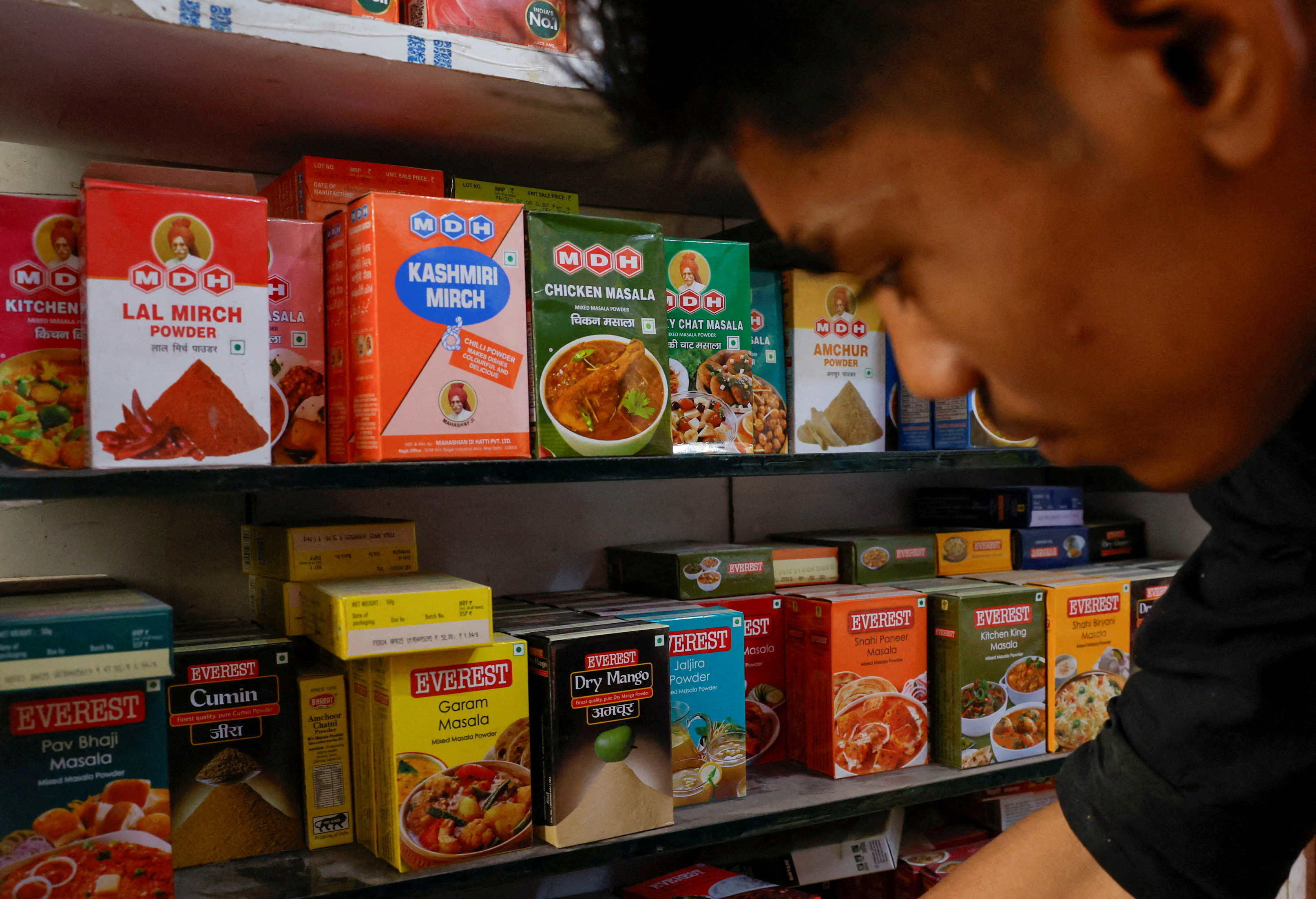 FILE PHOTO: FILE PHOTO: A man stands near the spice boxes of MDH and Everest kept on the shelf of a shop at a market in New Delhi