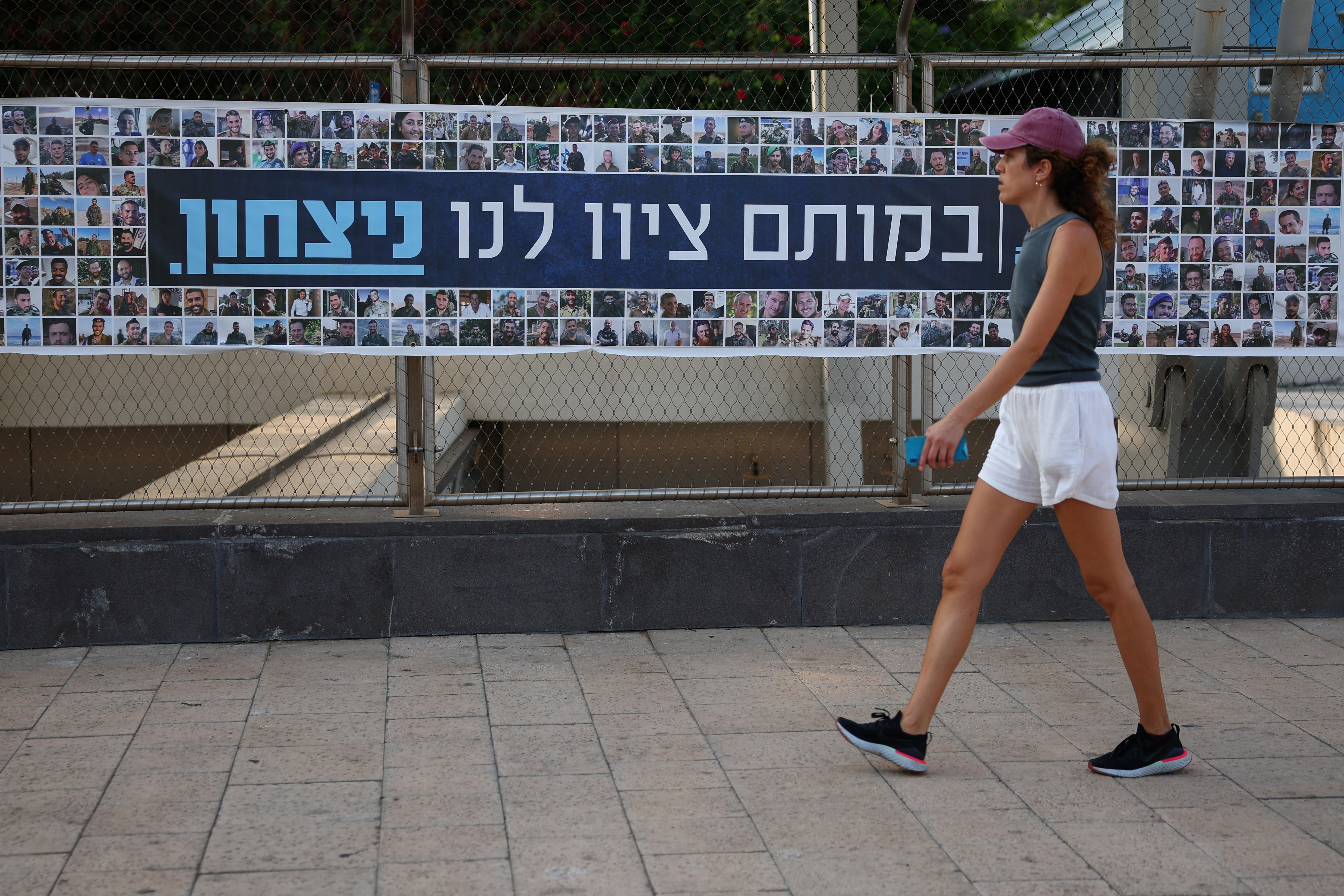 A woman walks past a banner depicting the faces of Israel’s fallen soldiers, amid the ongoing conflict in Gaza between Israel and Hamas, in Tel Aviv