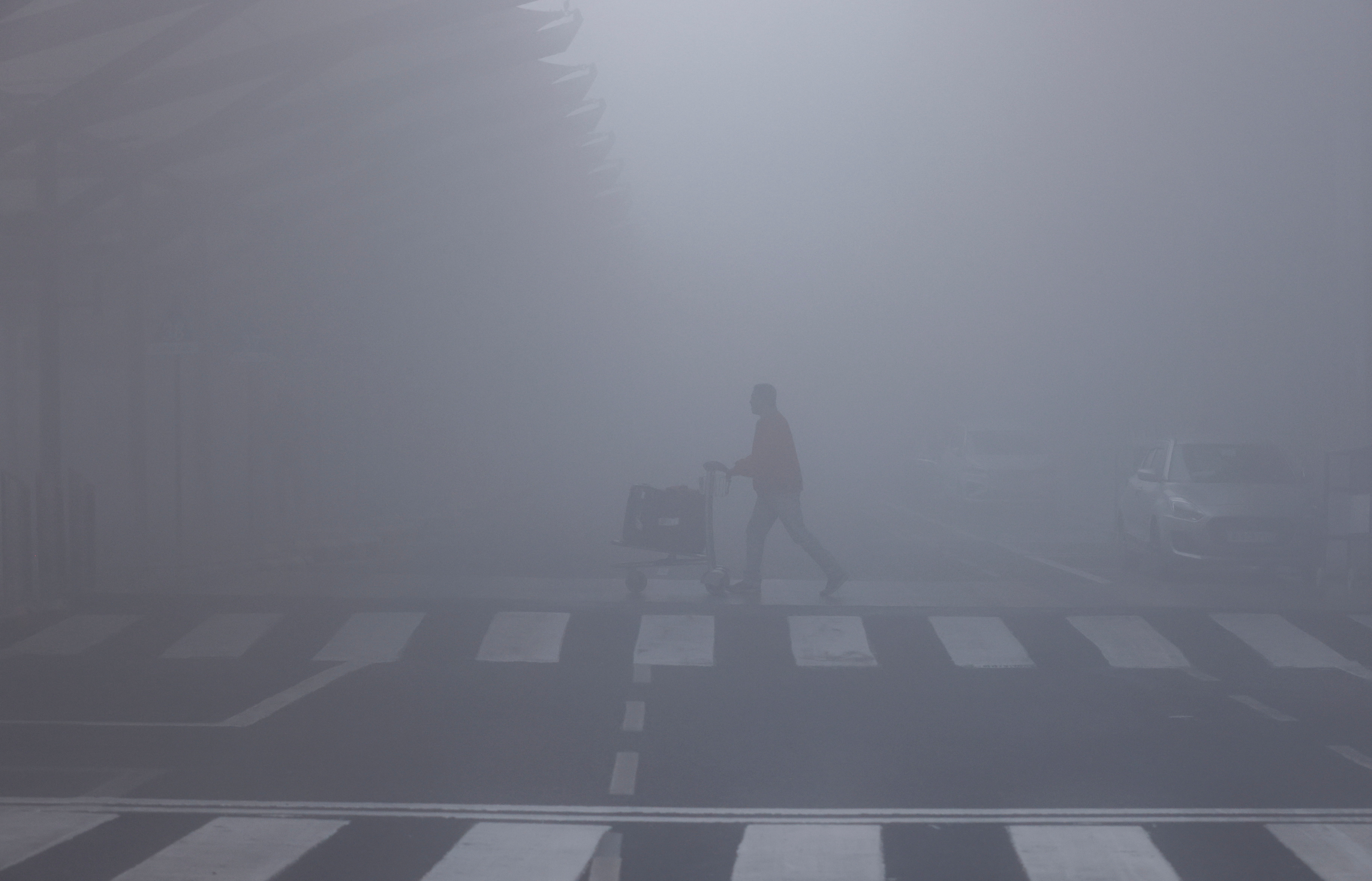 FILE PHOTO: A man walks with his luggage cart amidst heavy fog at the Indira Gandhi International Airport in New Delhi