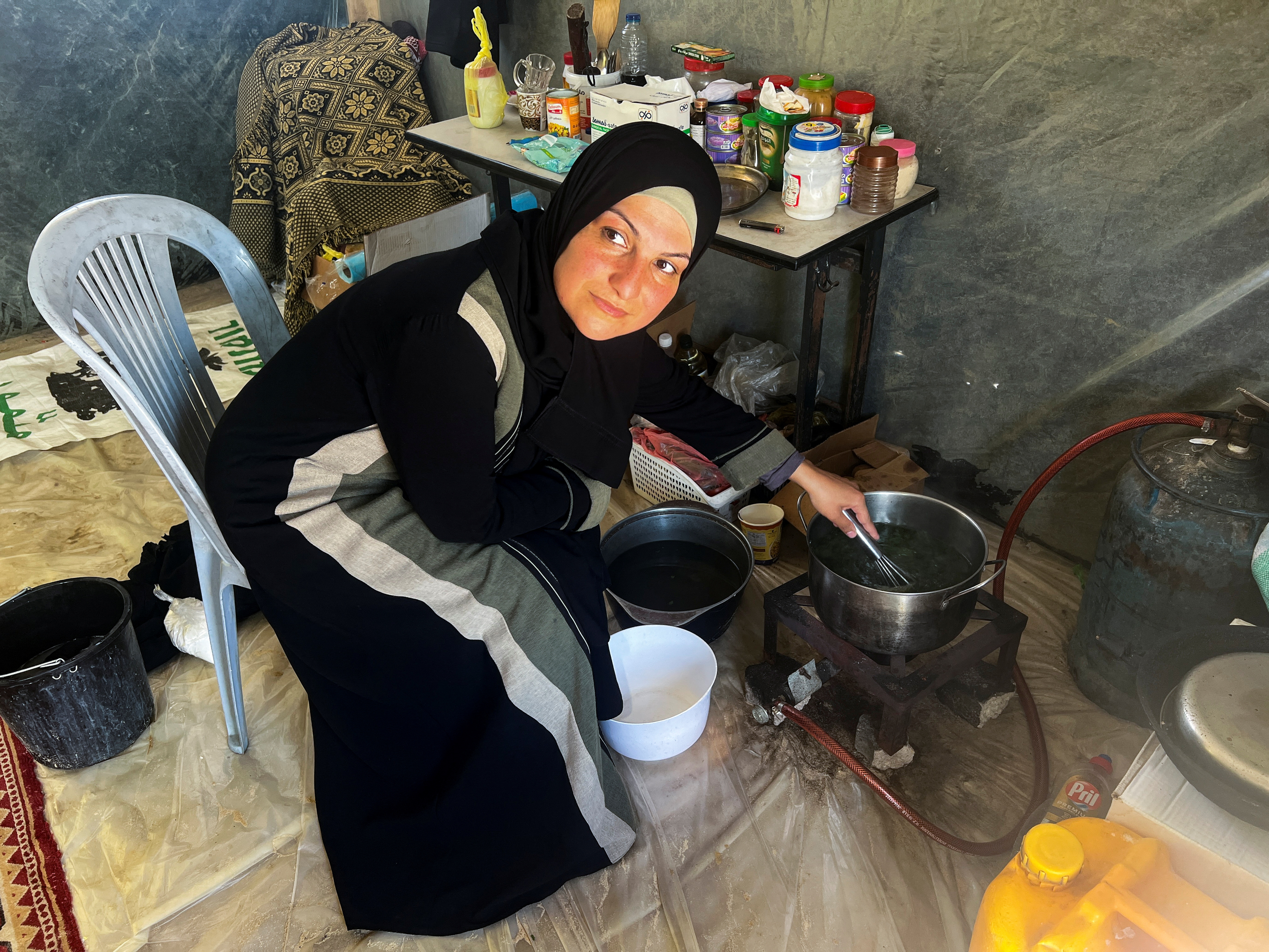 Inas Al-Baz, a displaced teacher from Beach refugee camp in Gaza City, cooks food inside her tent, in Rafah, in the southern Gaza Strip