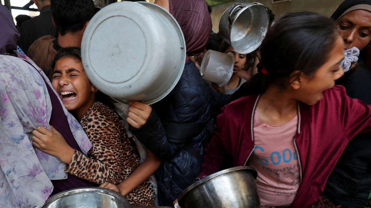 Palestinians wait to receive food cooked by a charity kitchen, in Gaza City