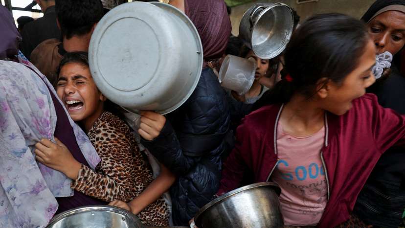 Palestinians wait to receive food cooked by a charity kitchen, in Gaza City
