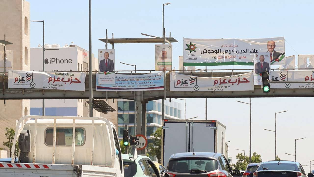 Cars pass near banners and pictures of candidates running in the country's parliamentary election in Amman