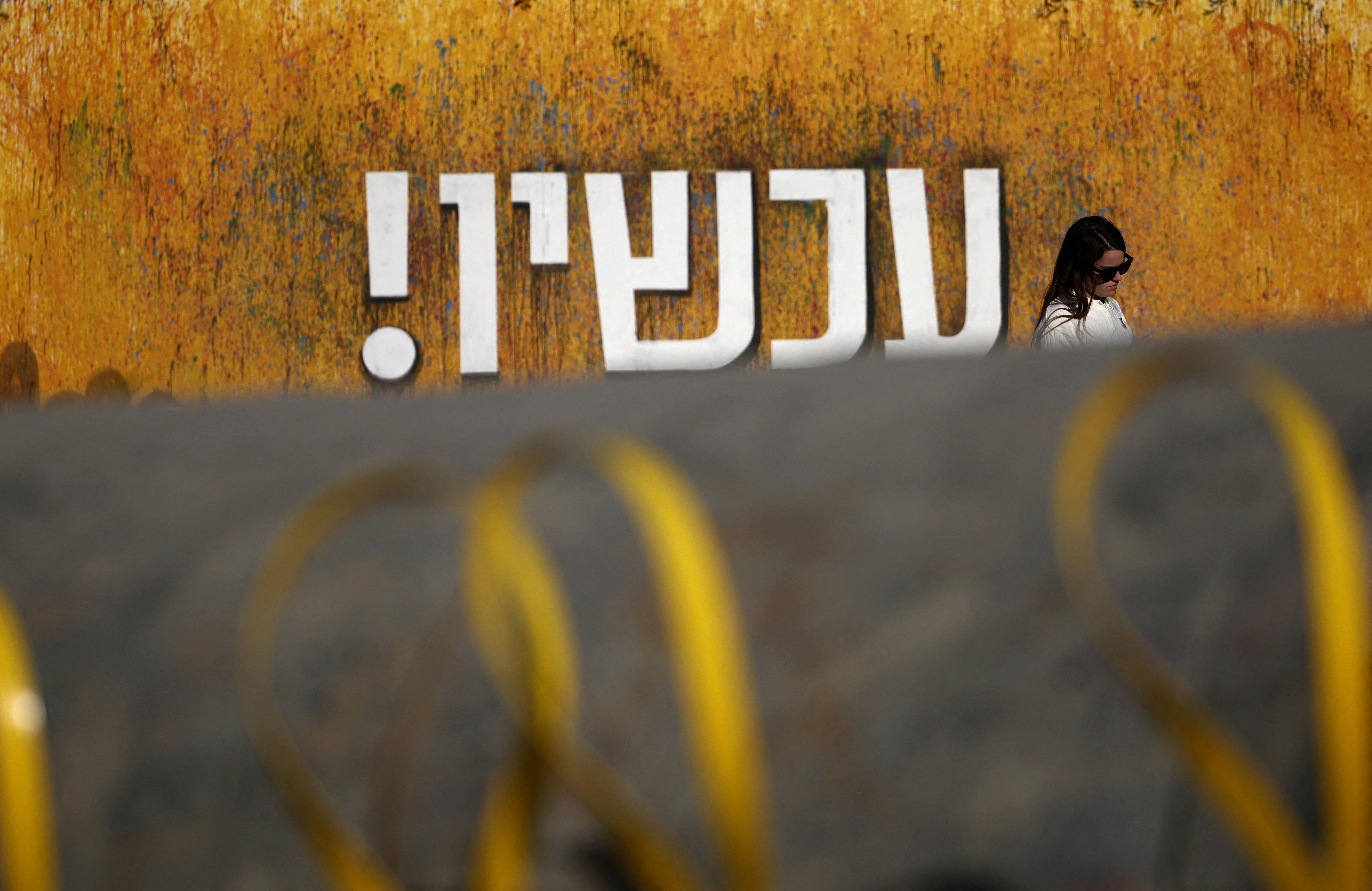 Woman walks near installation with yellow ribbons representing the struggle to release the hostages kidnapped during the deadly October 7, 2023 attack by Hamas, in Tel Aviv