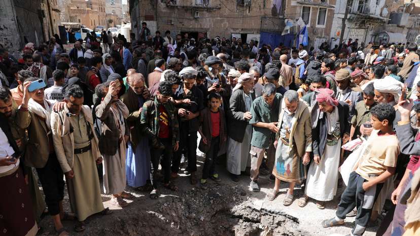 People gather around a crater at the site of a strike in Sanaa