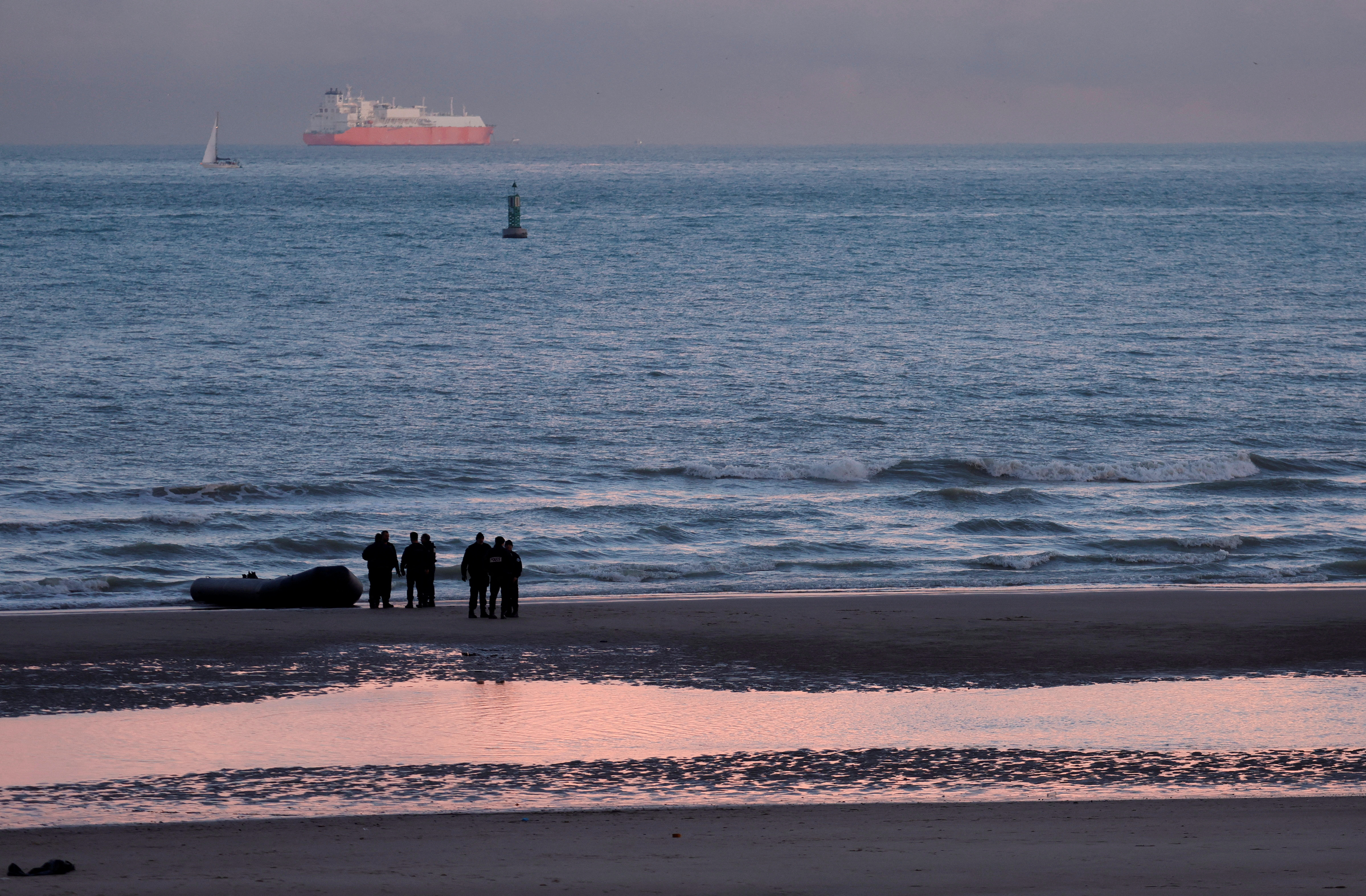 FILE PHOTO: French policemen stand beside a dinghy lying on the beach after migrants tried to reach Britain