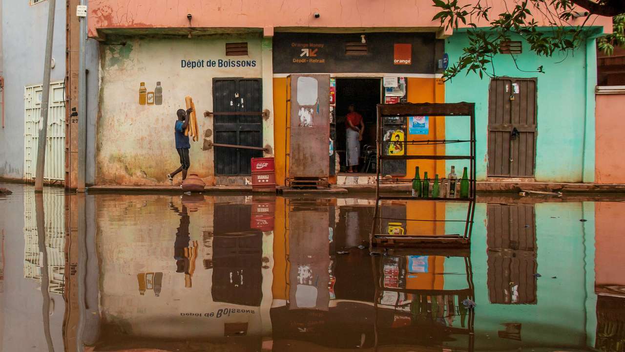 A man carries bread as he walks towards a grocery store, on a flooded street in Bamako