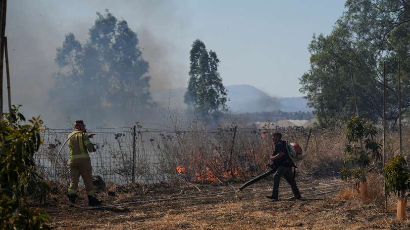 Israeli fire-fighter and another man work to take control over fire following rocket attacks from Lebanon