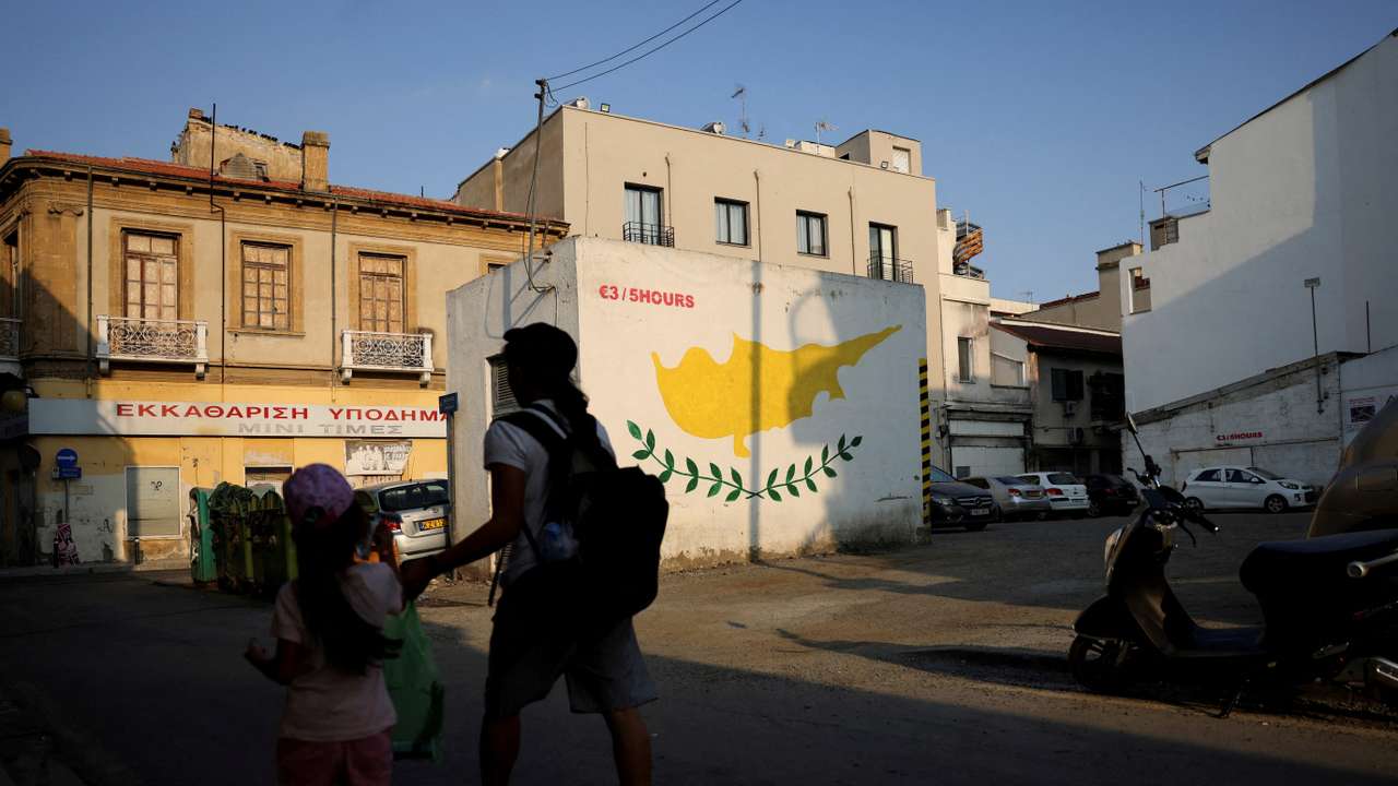 FILE PHOTO: People walk next to a Cypriot flag painted on a wall in Nicosia