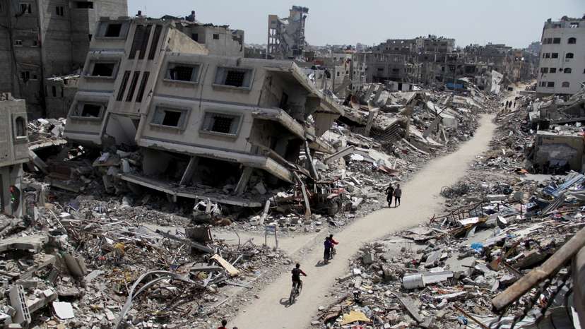 Palestinians ride bicycles past the ruins of houses and buildings destroyed during Israel’ military offensive, in the northern Gaza Strip