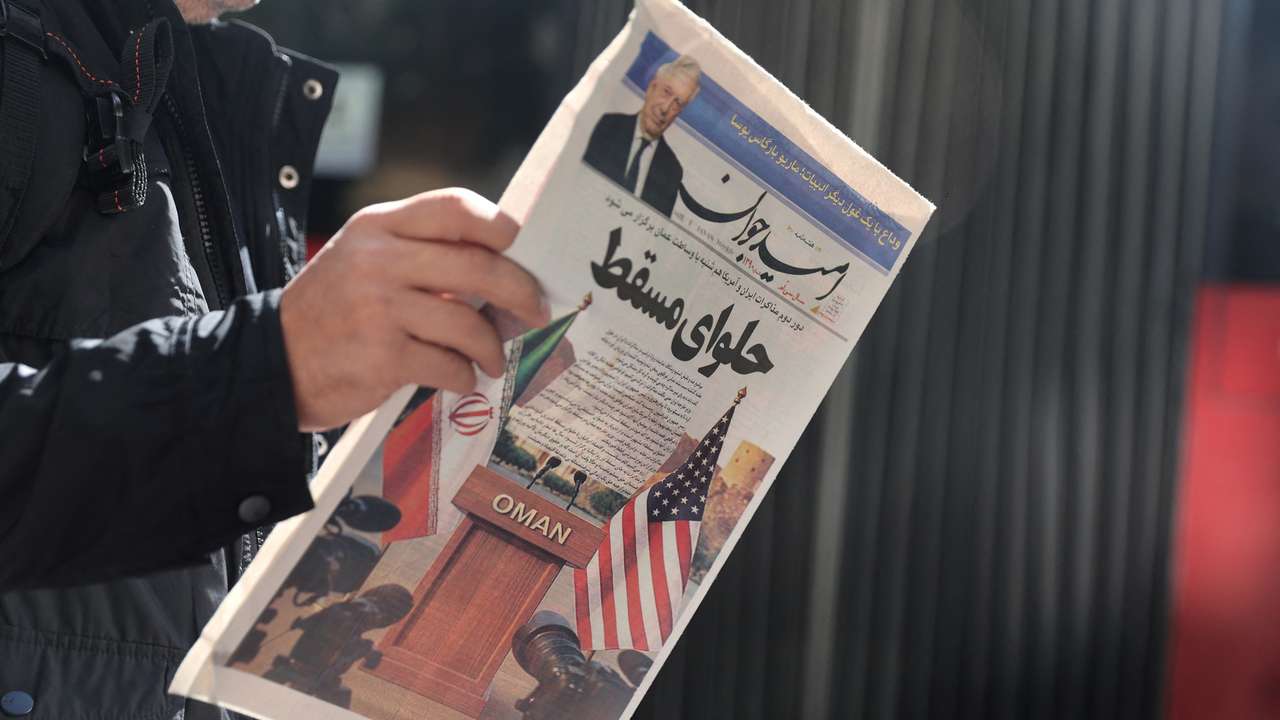 An Iranian man holds a newspaper with a cover photo of Iran and U.S. flags on a street in Tehran