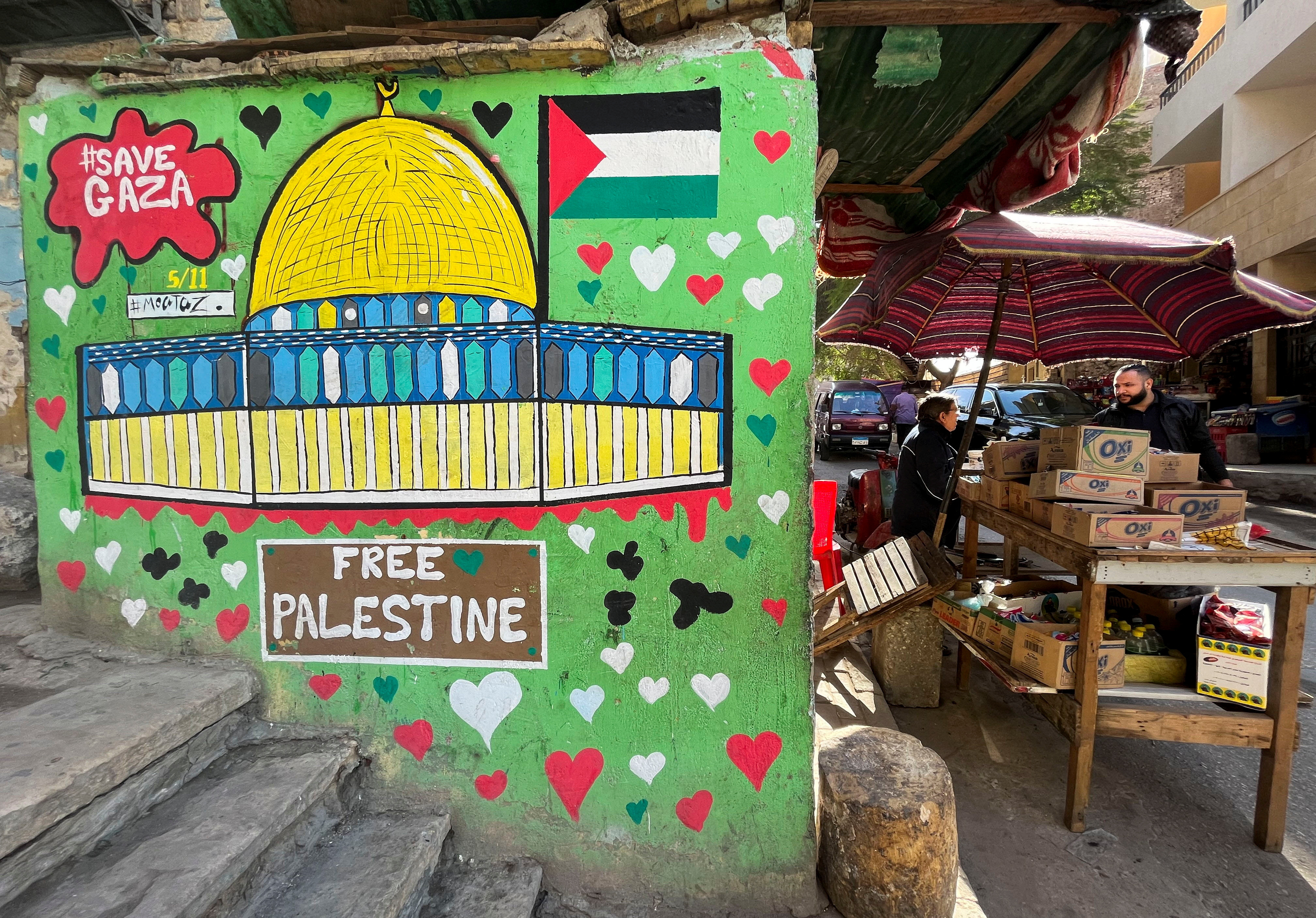 A vendor stands next to a mural in support of Palestinians in Gaza strip on a wall in Cairo