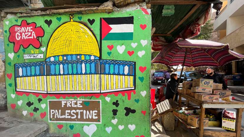 A vendor stands next to a mural in support of Palestinians in Gaza strip on a wall in Cairo