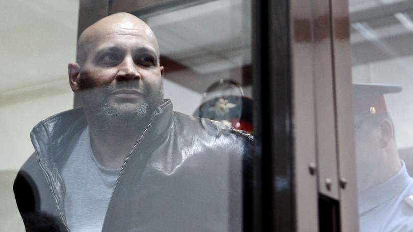 FILE PHOTO: Khadzhikurbanov is escorted into a glass-walled cage before a court hearing in Moscow