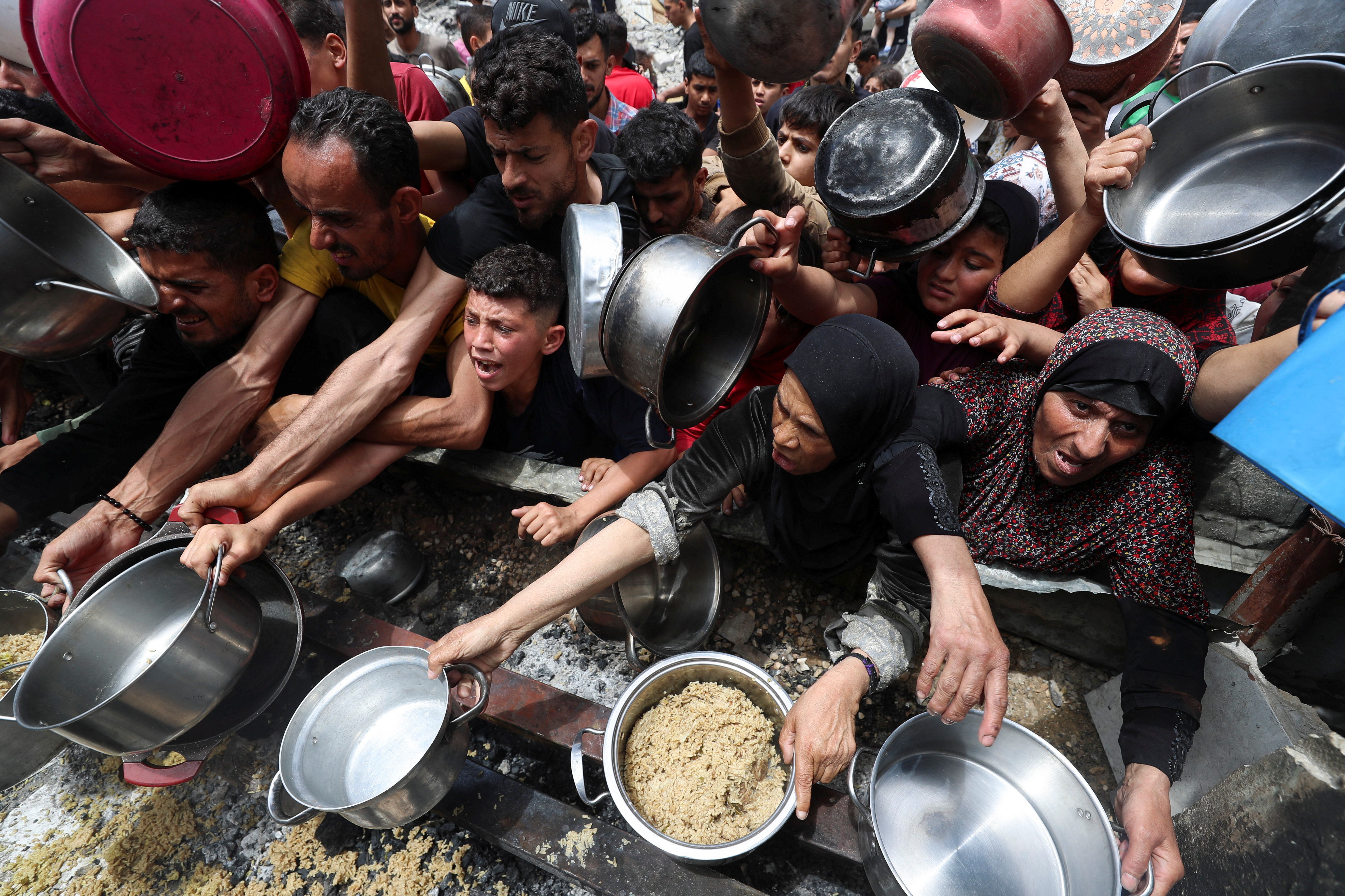 Palestinians wait to receive food cooked by a charity kitchen, in Jabalia