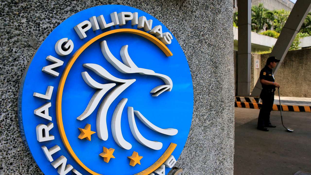FILE PHOTO: FILE PHOTO: Security guard stands beside a logo of the Bangko Sentral ng Pilipinas (Central Bank of the Philippines) posted at the main gate in Manila