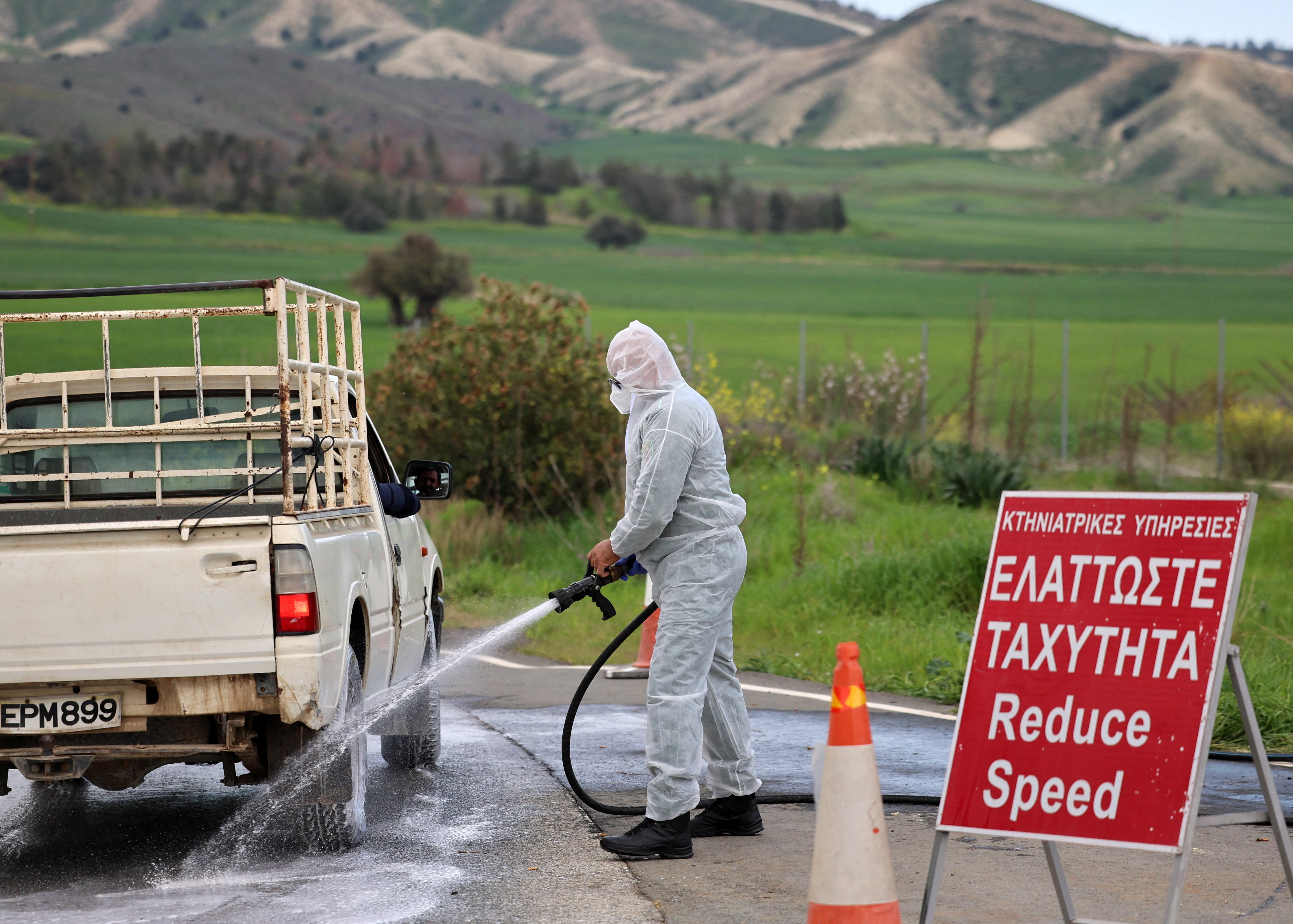 Man in a hazmat suit disinfects a vehicle and the road leading to farming units Oroklini, Cyprus, following cases of foot and mouth disease among livestock