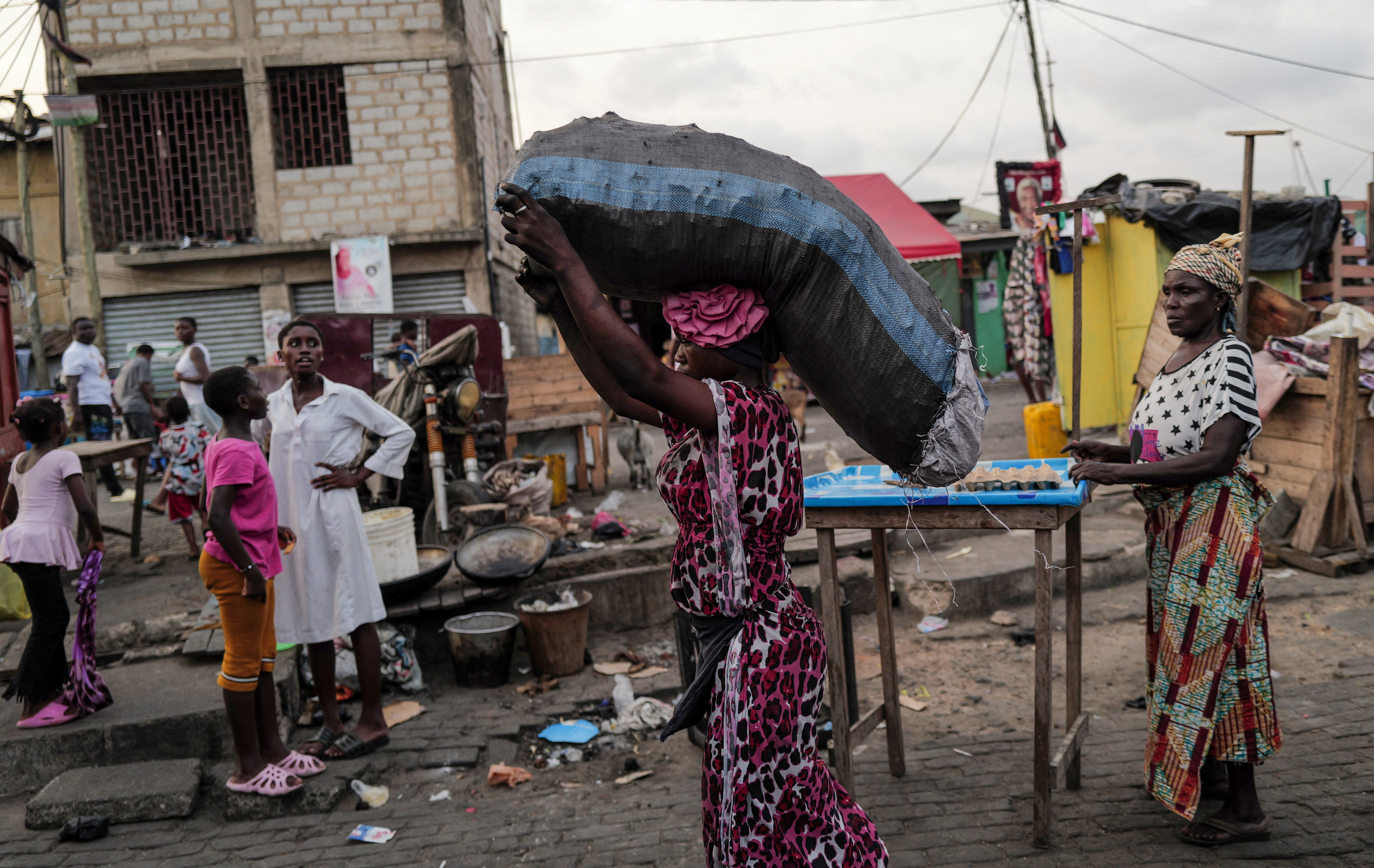 Woman carries sack of charcoal, as she walks down a busy street, in Jamestown in Accra