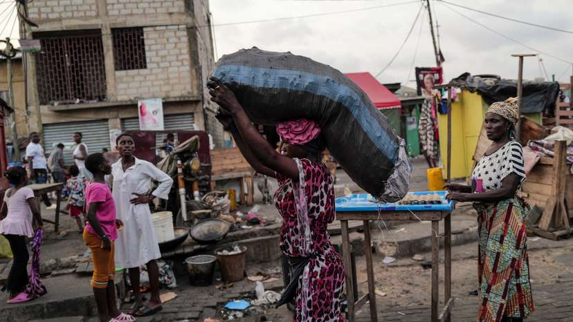 Woman carries sack of charcoal, as she walks down a busy street, in Jamestown in Accra