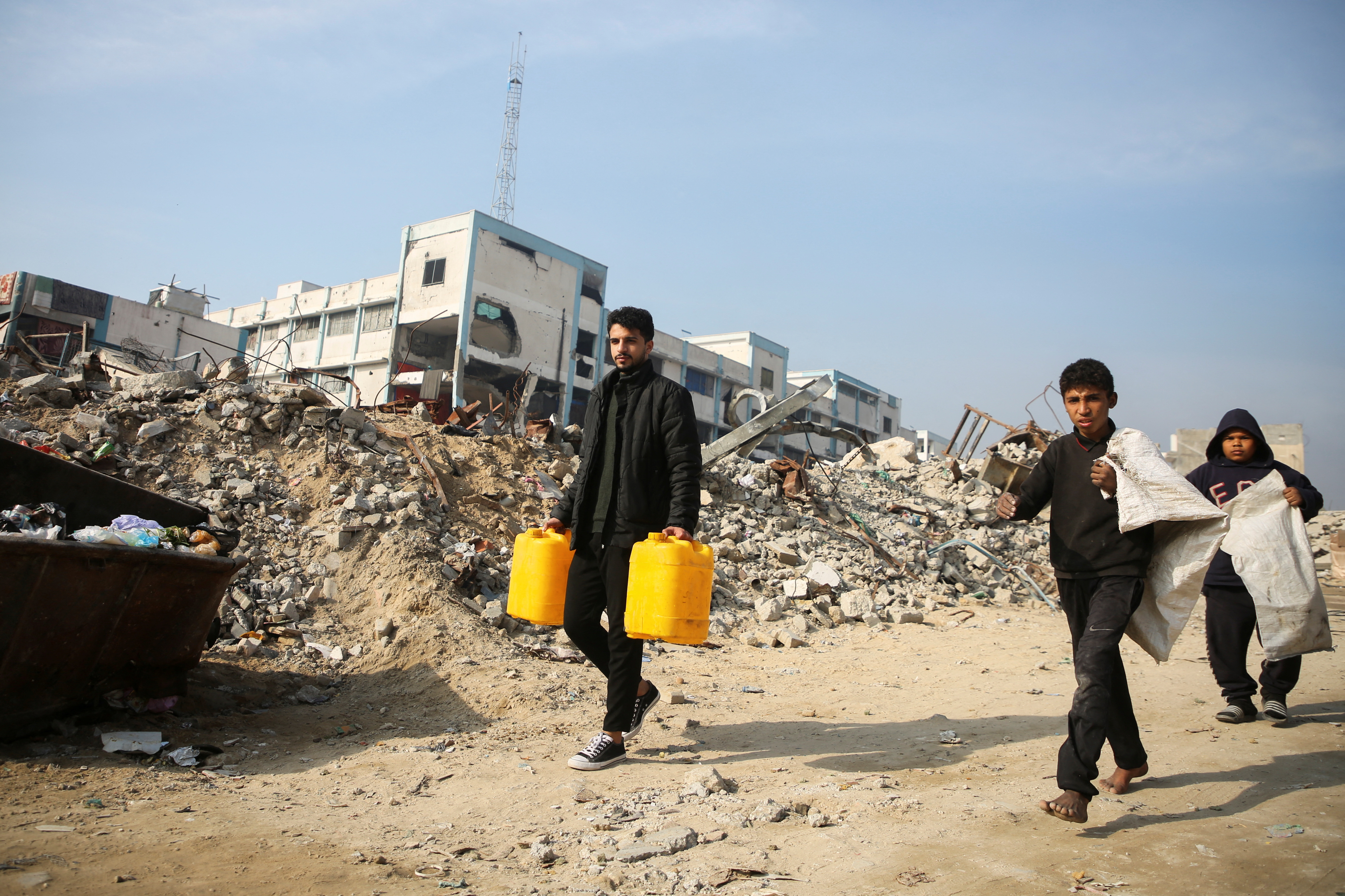 Palestinians walk past the rubble of buildings destroyed in previous Israeli strikes, ahead of a ceasefire set to take effect on Sunday, in Khan Younis