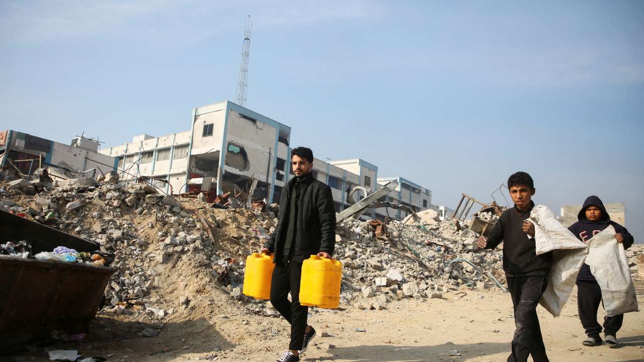 Palestinians walk past the rubble of buildings destroyed in previous Israeli strikes, ahead of a ceasefire set to take effect on Sunday, in Khan Younis