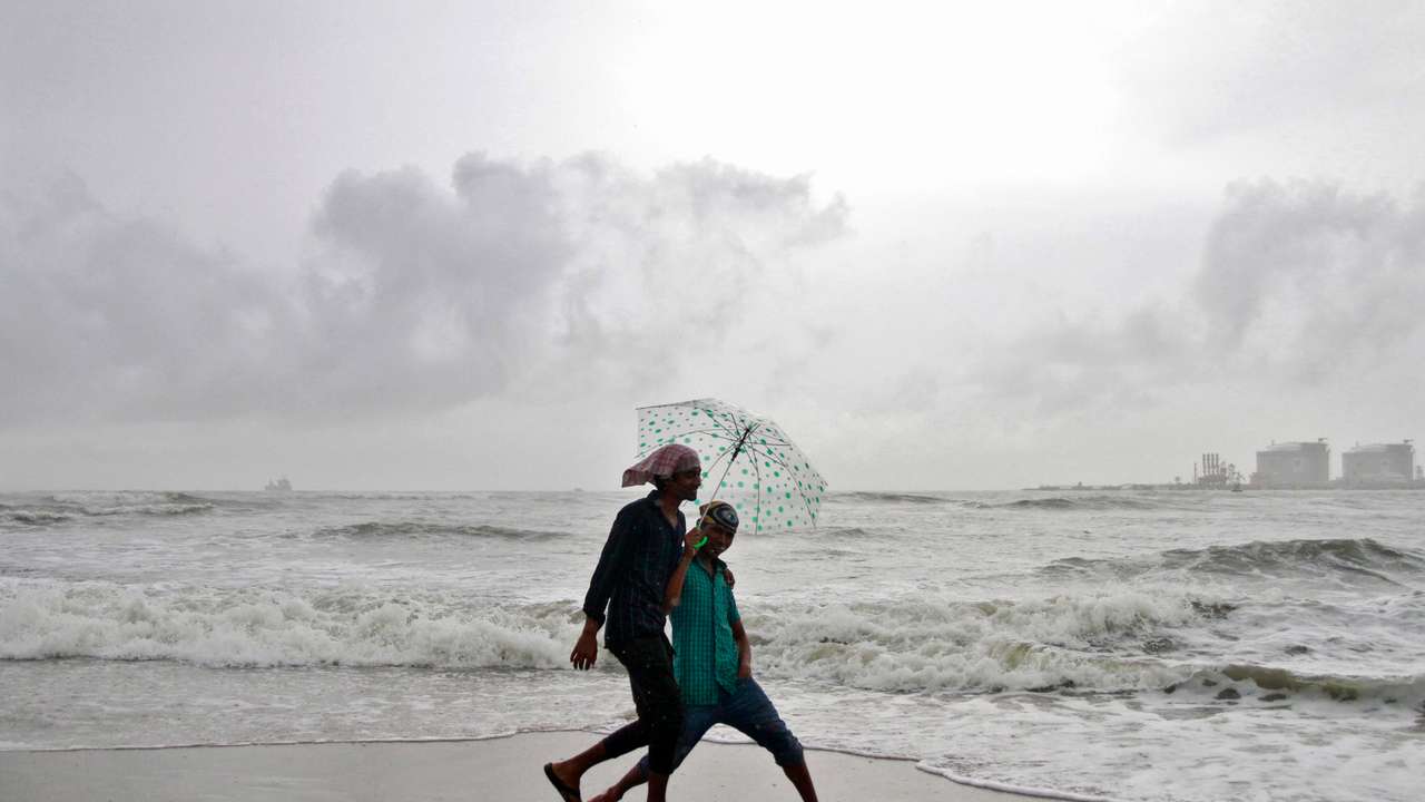 Beachgoers react to the camera while holding an umbrella as it drizzles at the Fort Kochi beach in Kochi