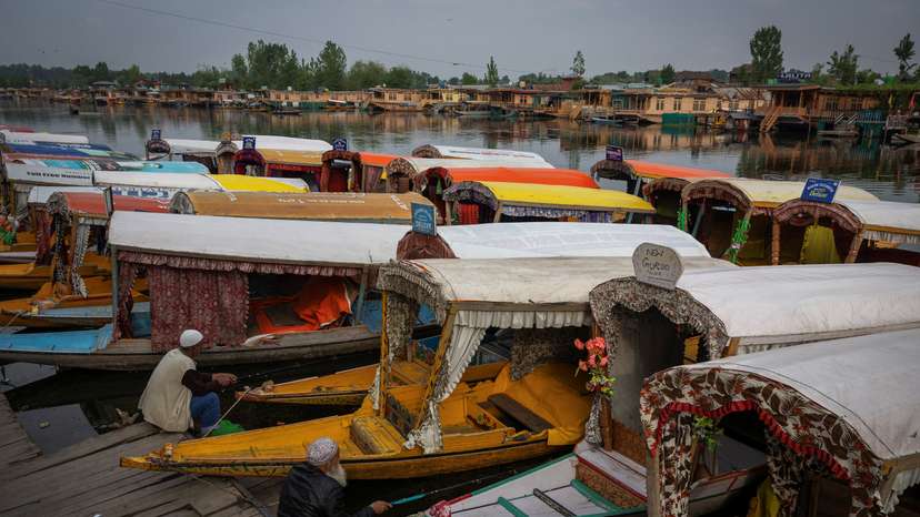 Kashmiri men catch fish as they sit next to parked "Shikaras" or boats on the banks of Dal Lake in Srinagar