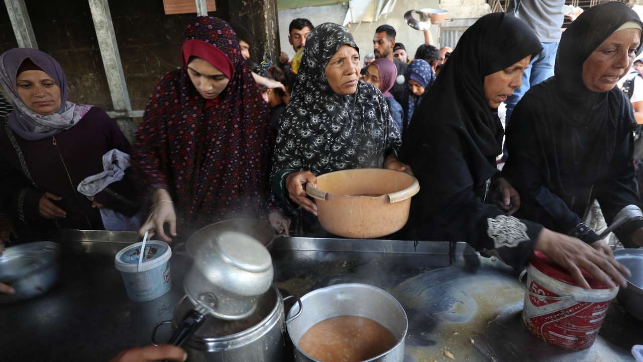 Palestinians wait to receive food cooked by a charity kitchen, in Gaza City