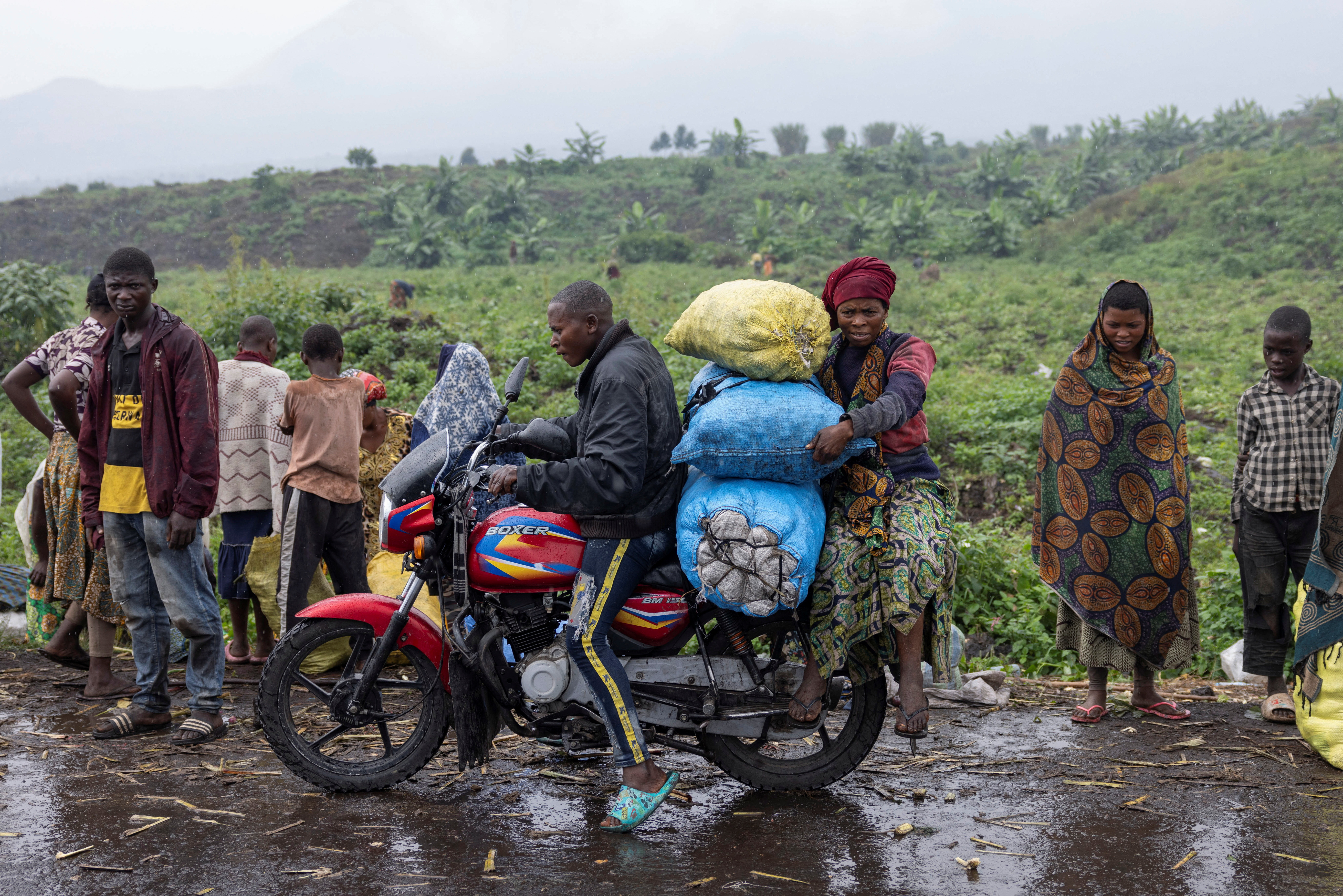 A person drives as another holds bags of potatoes from the Kibati market