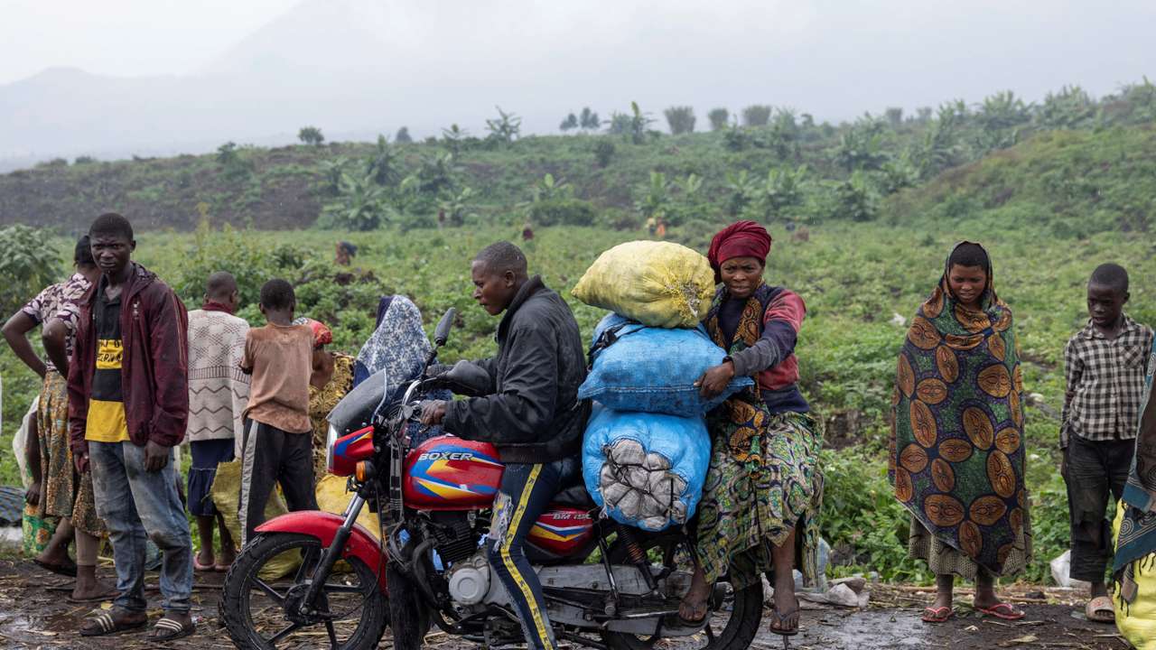 A person drives as another holds bags of potatoes from the Kibati market