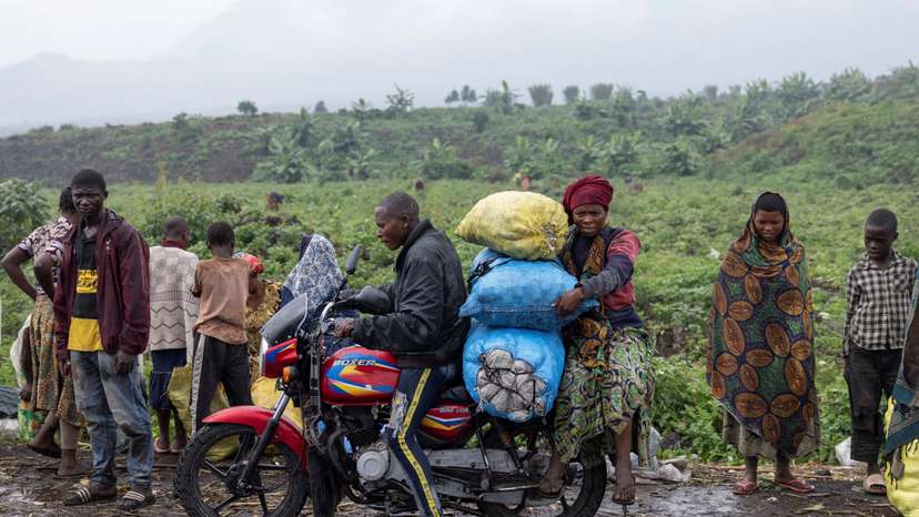 A person drives as another holds bags of potatoes from the Kibati market