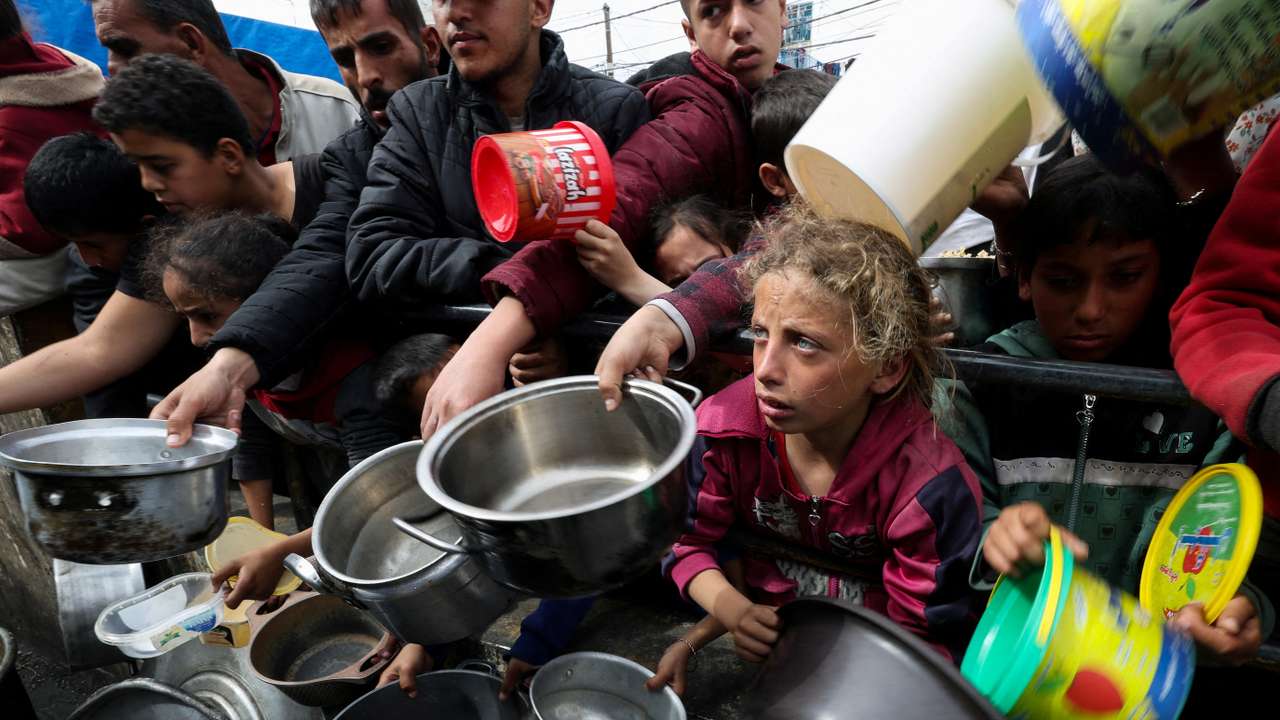 FILE PHOTO: Palestinian children wait to receive food cooked by a charity kitchen amid shortages of food supplies, in Rafah