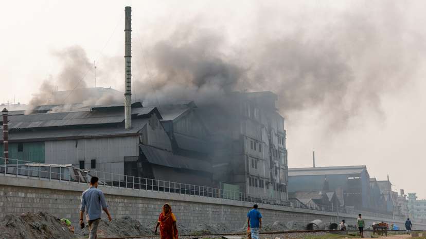 Commuters pass an industrial area as smoke rises from re-rolling factories at the Shyampur area of Dhaka