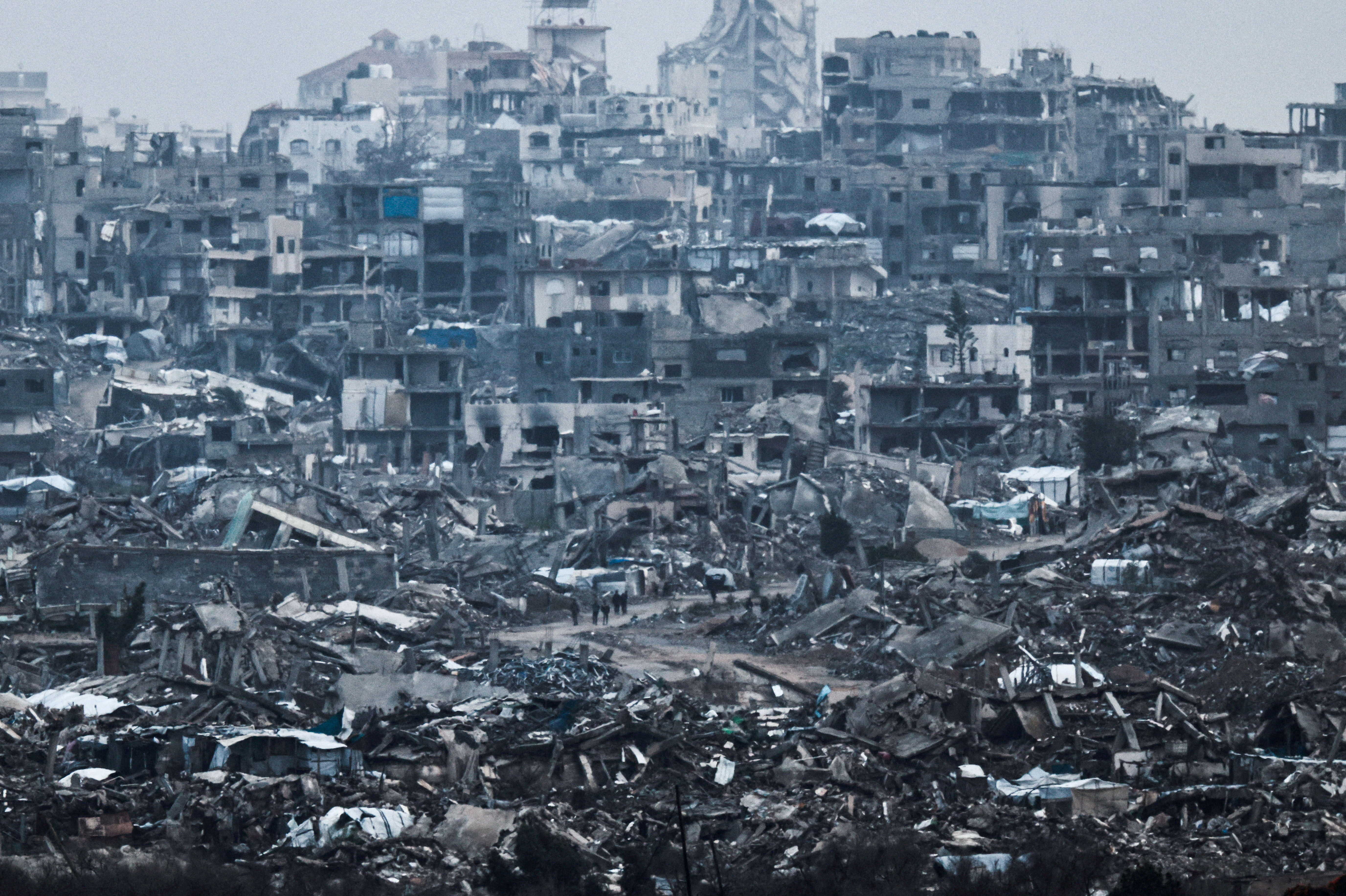 Palestinians walk near damaged buildings in the Gaza Strip, as seen from Israel