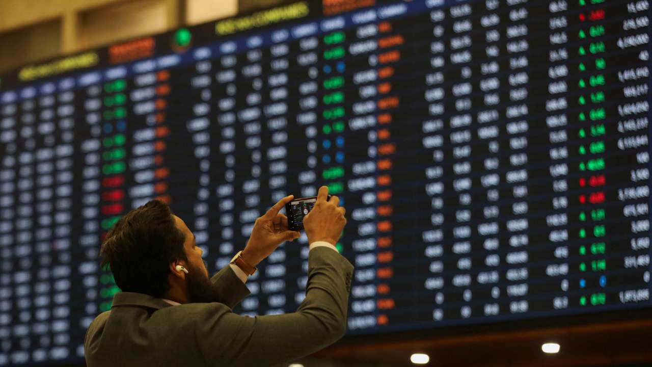 Man takes a photo of the electronic board displaying share prices during a trading session at the Pakistan Stock Exchange, in Karachi
